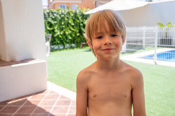 Portrait of a Cute smiling little boy standing near outdoor swimming pool