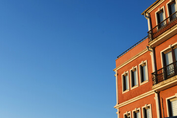 Orange Building Against Blue Sky. A vibrant orange building with geometric lines contrasting against a clear blue sky, capturing sunlight and offering ample space for text.