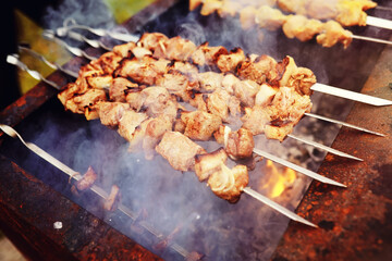 Selective focus. Cooking barbecue on the mangal in nature. Grilled tasty meet cooking on the party. Traditional Russian shashlik on a barbecue skewer on sunny forest.