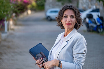 Fototapeta premium Business woman or young professor sitting in front of office building or university campus and holding a file and looking at the camera.