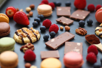 Macarons, chocolate, cookies, berries and various nuts on dark blue background. Selective focus.