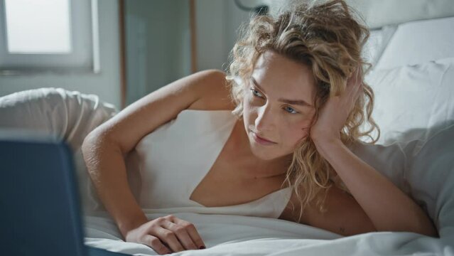 Relaxed woman watching computer online. Closeup serene girl lying on cozy bed