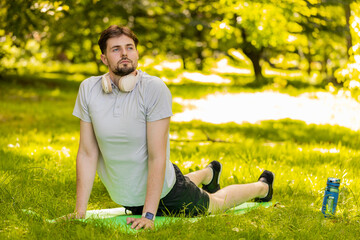 Fototapeta premium Fit flexible man doing workout yoga stretching on a sports mat in park. Raising head. Young male guy enjoying exercising outdoors. Active sportsman motivation. Determined athlete healthy lifestyle.