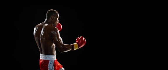 Muscular man with strong body, boxer in motion, fighting isolated on black background isolated on...