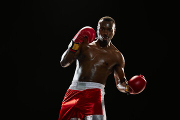 Muscular serious man, boxer with shirtless and sweating body training, punching isolated on black...