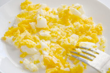 Mashed egg with a fork on a white plate. 