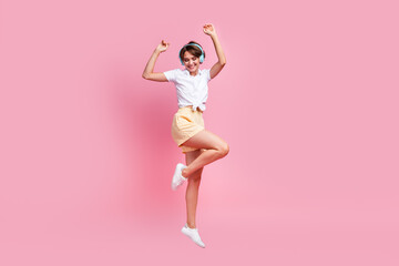 Full view shot of attractive youth girl listening her favorite retro music use modern headphones jumping isolated on pink color background