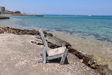 A tranquil view of the beach, an old wooden chair and a crystal clear ocean. For themes of peace, loneliness and beauty of nature, summer and travel photography