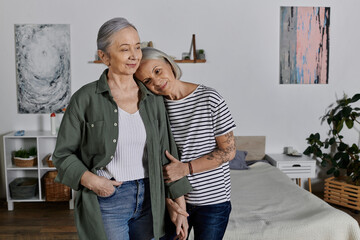 Two mature women, an older lesbian couple, stand together in a modern apartment, embracing each other lovingly.