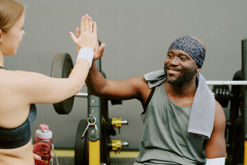 African American man sitting on bench and high fiving his sporty and active gym crush
