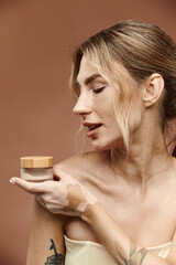 A woman with vitiligo holds cream, gazing thoughtfully, against a beige backdrop.