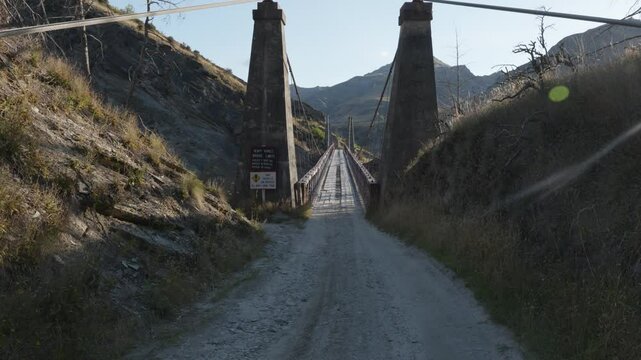 A dirt road leading to an old bridge above a valley on a sunny summer day at Skippers Canyon, Queenstown, New Zealand.