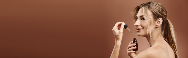 Naklejka premium A young woman with vitiligo applies a skincare product to her face against a beige backdrop.