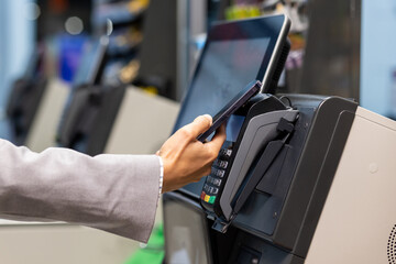 Closeup image showcasing a person using a smartphone for contactless payment at a point of sale terminal in a retail store. The concept convenience increasing usage of mobile payment methods.