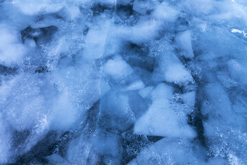 Abstract natural background of ice surface of frozen Baikal Lake on cold winter day. Pieces of ice floes stuck into thickness of blue ice. Unique icy pattern. Top view, close-up, mock up, flat lay