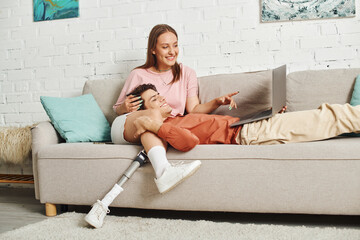 A woman with a prosthetic leg and her boyfriend are relaxing on a sofa, sharing a laugh together.