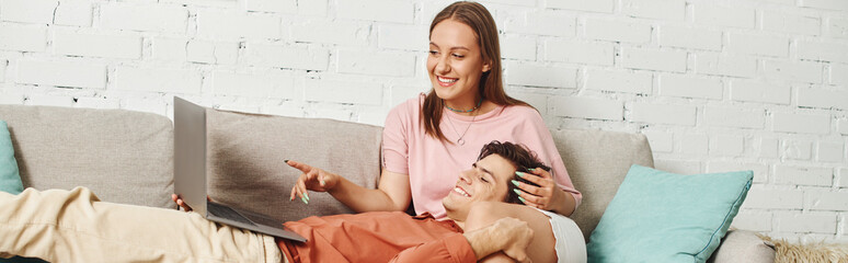A woman with a prosthetic leg cuddles with her boyfriend on a couch while looking at a laptop.