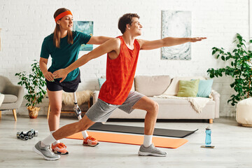 A woman with a prosthetic leg helps her boyfriend with his workout routine at home.