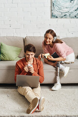 A woman with a prosthetic leg sits on a couch, while her boyfriend works on his laptop.