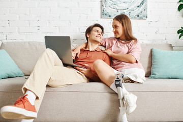 Couple on couch, woman with prosthetic leg, sharing intimate moment.