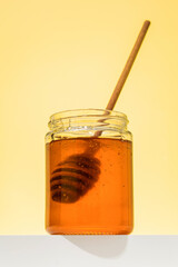 Golden floral honey in a jar with a wooden ladle on the podium. Organic and healthy.