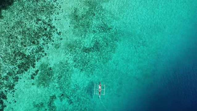 Fishing boat sailing over a coral reef in the crystal clear water of the ocean aerial view
