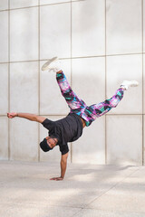 Young man wearing streetwear is breakdancing upside down balancing on one hand in the street