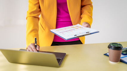 An Asian businesswoman is diligently working at an accountant's desk, surrounded by financial...