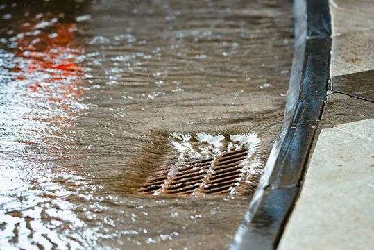 Rainwater flowing over highway storm drain grate. Floodwater and drainage on roads during heavy rain. Flooding on city road with water flowing into storm drains. Sewage management. Selective focus