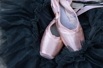Closeup of the pink ballet pointe shoes laying on the black chiffon Tutu. Two beige ballet slippers on the dark background. Minimalistic concept. Copy Space. Selective focus. © Dina