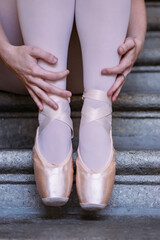 Closeup of ballerina's pointes on the gray stone steps background. Dance sitting on the steps. Ballerina´s feet with pink ballet slippers on. Minimalistic, simple. Copy space. © Dina