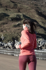 A woman in pink activewear jogging along a beach, with rocky cliffs in the background on a sunny day.