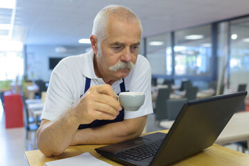 elderly cafeteria worker drinking coffee readin laptop