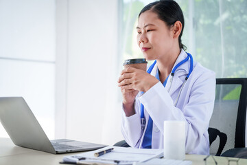 An Asian female doctor sits at her desk, conducting an online consultation. This faster, cheaper, and more convenient method helps prevent disease spread and offers easier access to healthcare.