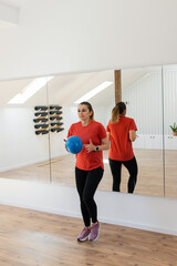 Obraz premium Woman In A Fitness Studio Performing An Exercise With A Blue Ball, Reflected In A Large Mirror 