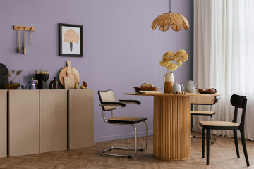 Warm and cozy dining room interior with mock up poster frame, round table, rattan chairs, beige commode, lamp, vase with flowers, kitchen cutboard and personal accessories. Home decor. Template.