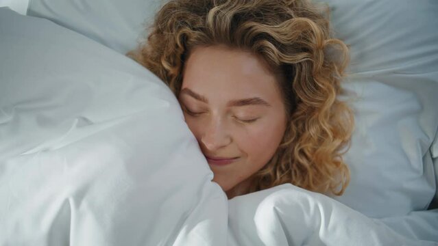 Happy blonde resting pillow hiding under blanket closeup. Smiling woman dreaming