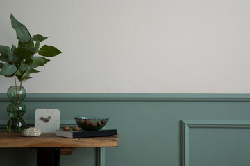 Minimalist composition of living room interior with copy space, wooden bench, clock, glass vase with leaves, bowl with nuts, book, beige wall and personal accessories. Home decor. Template.