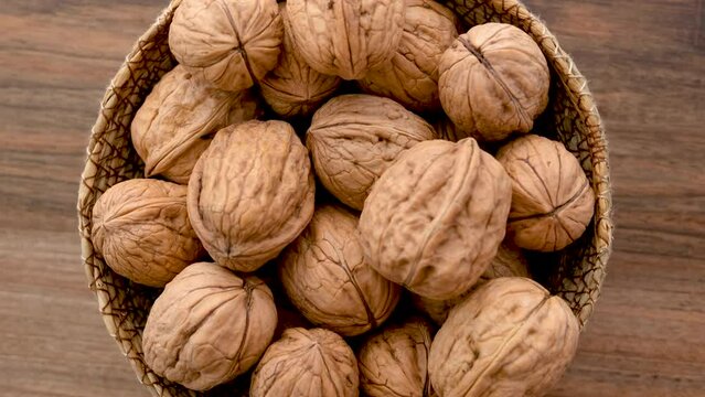 Close-up view of a wicker bowl filled with shelled walnuts rotates on a wooden surface