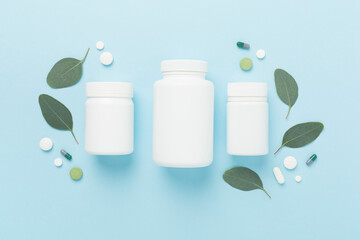 Bottle with pills and green leaves on color background, top view