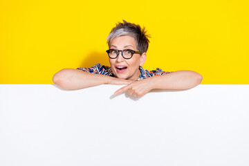 Photo portrait of lovely senior lady point down empty space dressed stylish colorful garment isolated on yellow color background