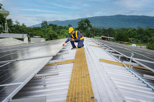 An engineer with a tablet and utilizing radio communication, meticulously inspects solar panels on a rooftop. These panels are integral to a smart grid ecosystem.