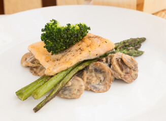 Dish of fried river trout fillet with garnish of broccoli, asparagus sprouts and mushroom sauce on white background