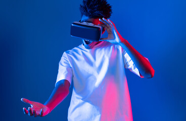 Surprised young African American looking through VR holding interesting object hologram on pink...