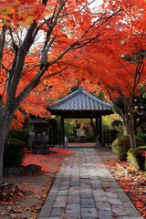 A path covered with fallen red maple leaves leads to a traditional Japanese temple gate