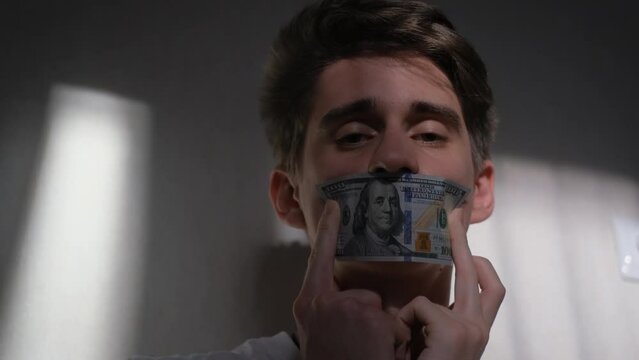 A man covers his mouth with a dollar bill. Concept: bribery, blackmail, perjury