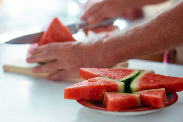 Close-up view of senior people's hands cutting a red juicy watermelon in slices, healthy and refreshing snack
