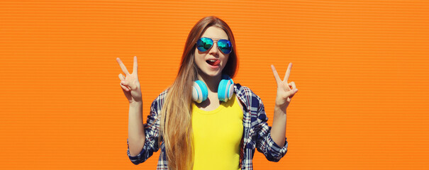 Stylish young woman listening to music with headphones, modern teenager girl posing on orange wall