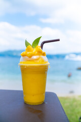 Smoothie made from fresh mango fruits against the backdrop of a seascape. Fruit and yoghurt ice cream decorated with leaves. Glass of tropical dessert close-up.