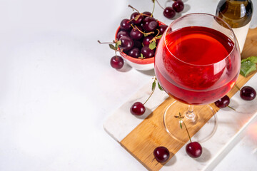 Sweet alcohol cherry wine drink, homemade cherry wine or liquor with ripe fresh red cherries on kitchen table copy space